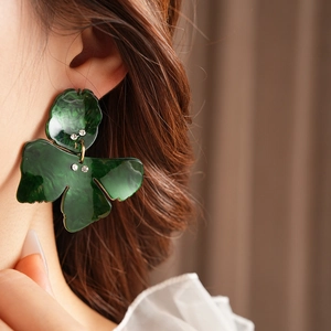 Close-up of green resin leaf earrings with sparkling rhinestone studs on a female model