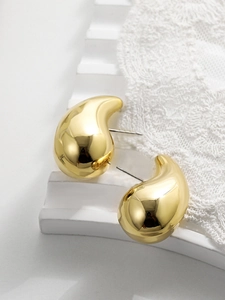 Close-up of gold teardrop earrings with high-gloss finish on a white textured stand