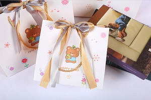 Detail of cartoon bear gift bag featuring gold braided handles and silky satin ribbons