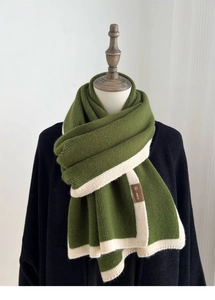 Detail of army green knitted scarf with cream border and leather brand tag on wood mannequin