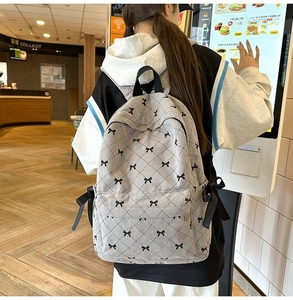 Beige corduroy backpack with black bows and ribbon detail worn in a casual lifestyle setting