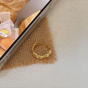 Minimalist irregular wave-shaped gold ring with liquid metal texture on linen fabric