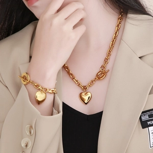 Close-up of golden heart pendant necklace and bracelet set with OT toggle clasp on model