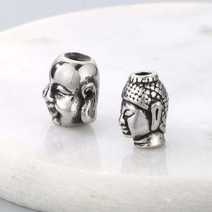 Macro shot of silver stainless steel Buddha head spacer beads on white marble base