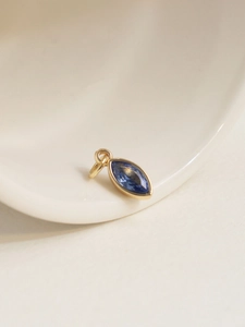 Macro view of a gold-plated oval pendant with marquise-cut blue zircon on a ceramic tray