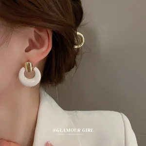 Detail of white C-shaped hoop earrings with gold metal studs on a model wearing a blazer
