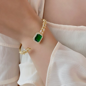 Detail of emerald green zircon gold open bangle bracelet on model's wrist