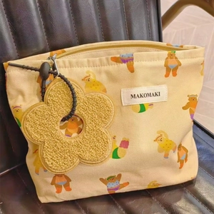 Detail of beige canvas makeup bag with cartoon bear pattern and yellow floral plush charm