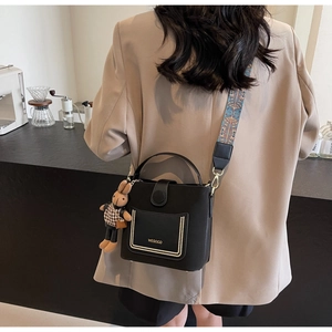 Macro detail of black leather bucket bag with wide ethnic strap and plush rabbit charm
