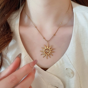 Dettaglio di una collana con ciondolo a sole dorato e perline indossata da una modella