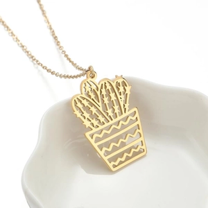 Golden stainless steel cactus pendant necklace displayed on a white wavy ceramic plate
