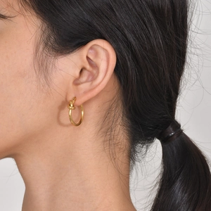 Detailed view of model wearing gold knot earrings with polished stainless steel finish
