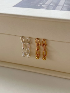 Detail view of gold and silver U-shaped chain link earrings on a gift box edge