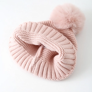 Detail of the pink winter knitted beanie featuring a large fluffy faux fur pom-pom on top