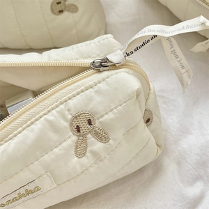 Detailed macro view of cream quilted fabric pouch featuring cute rabbit embroidery
