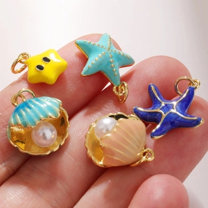 Macro view of ocean starfish and shell pendants with pearls held in hand for scale