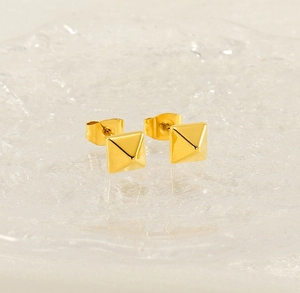 Gros plan de boucles d'oreilles pyramides en acier plaqué or 18k sur verre texturé