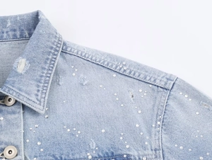 Détail de la veste en jean bleu clair avec ornements en perles et design d'épaule vieilli