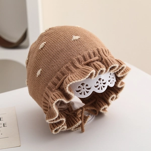 Dettaglio cappello neonato a maglia con pois marroni e bordo a volant con laccetti