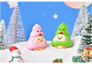 Close-up of pink and green resin chick figurines in Christmas tree costumes on snowy scene