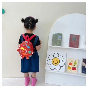 Detail of child wearing a red backpack with colorful cartoon dinosaur prints