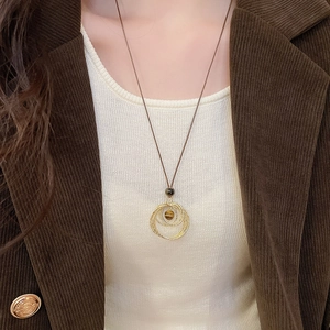 Detailed close-up of tiger eye stone pendant on brown cord necklace worn with corduroy blazer
