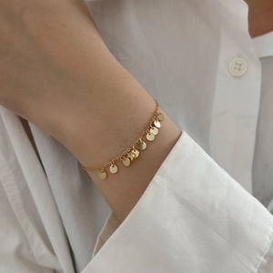 Close-up of a minimalist gold sterling silver bracelet with delicate round charms on wrist