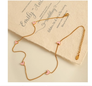 Detailed macro view of golden necklace chain featuring five delicate pink heart pendants