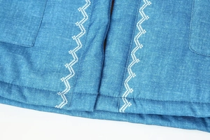 Close-up of white wavy embroidery on the placket and pocket of blue denim jacket