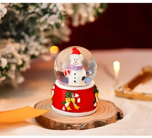 Close-up of a festive Christmas snowman snow globe with a red base on a rustic wood slice
