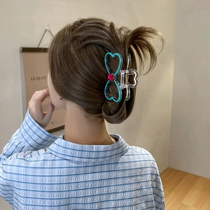 Blue rhinestone bow hair claw clip holding a brunette hair bun in a cozy home setting