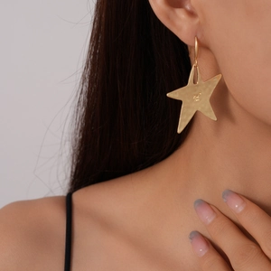 Detail of model wearing a golden star earring with a unique hammered texture surface