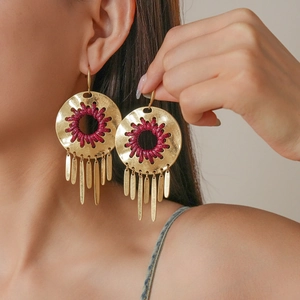 Detail of round woven tassel earrings with red thread accents on a female model