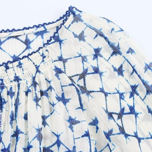 Dettaglio della camicetta blu e bianca tie-dye con strisce dorate e scollo intrecciato