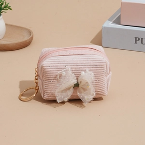 Pink corduroy mini coin purse with lace bow, pearls, and a golden keychain on warm background
