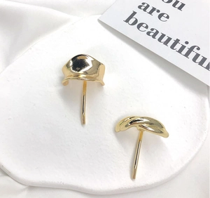 Close-up of 18K gold irregular geometric dome and knot earrings on a stone base