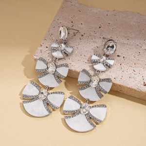 Elegant silver bow and fan-shaped earrings with rhinestones on a decorative stone