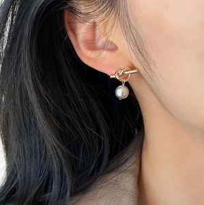 Elegant gold knot earrings with a silver-grey pearl pendant shown on an ear model