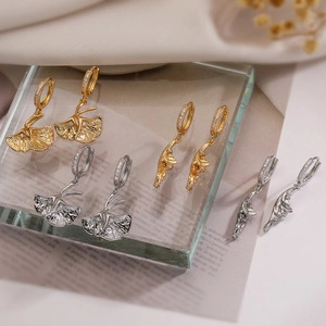 Detail shot of gold and silver ginkgo leaf earrings with zircon on a glass brick