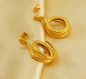 Macro detail of gold-plated snake earrings with scale texture on champagne silk fabric