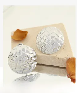 Macro shot of silver-tone round stud earrings with intricate woven texture on stone