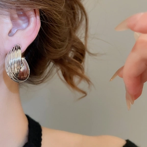 Close-up of a model wearing large silver-tone textured twisted hoop clip-on earrings