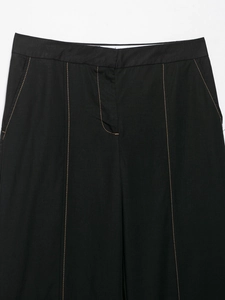 Detail of black straight trousers with contrast orange topstitching and functional pockets
