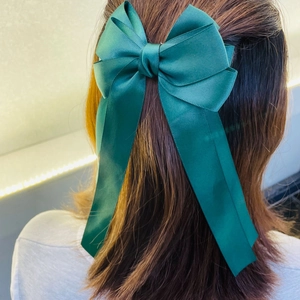 Detail of a green ribbon bow hair clip with long streamers on dark brown hair