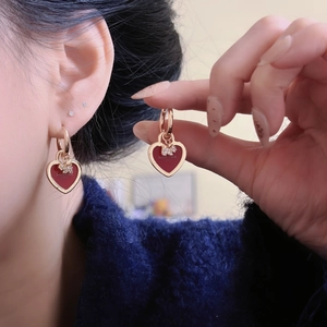 Détail de boucles d'oreilles cœur en or rose avec émail rouge et cristaux sur modèle