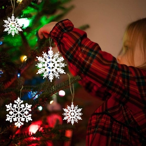 White snowflake ornaments with gold strings being hung on a decorated Christmas tree