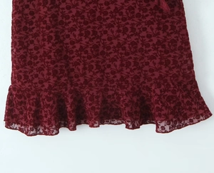 Detail of ruffled hem on wine red sleeveless dress with elegant rose floral patterns