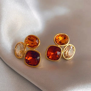 Detailed view of vintage geometric stud earrings with amber and red gemstones on satin fabric.