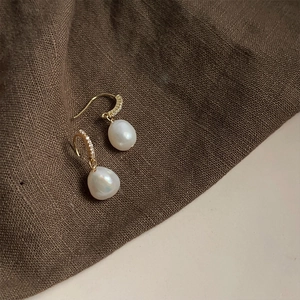 Macro detail of Baroque pearl earrings with sparkling gold pave diamond hooks