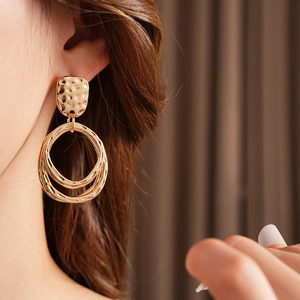 Detail of golden hammered geometric earrings with concentric rings on a female model
